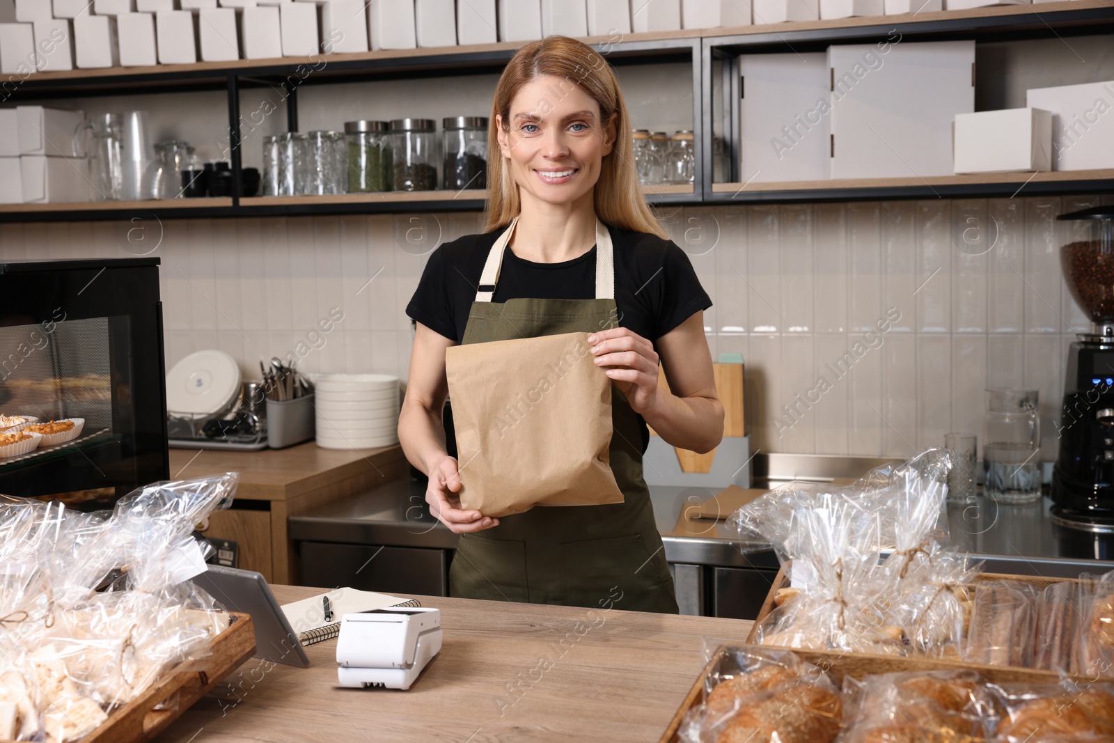 Photo of Happy seller with paper bag at cashier desk in bakery shop