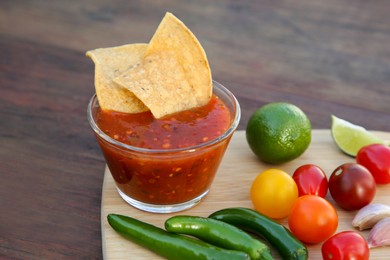 Tasty salsa sauce with tortilla chips and ingredients on wooden table, closeup