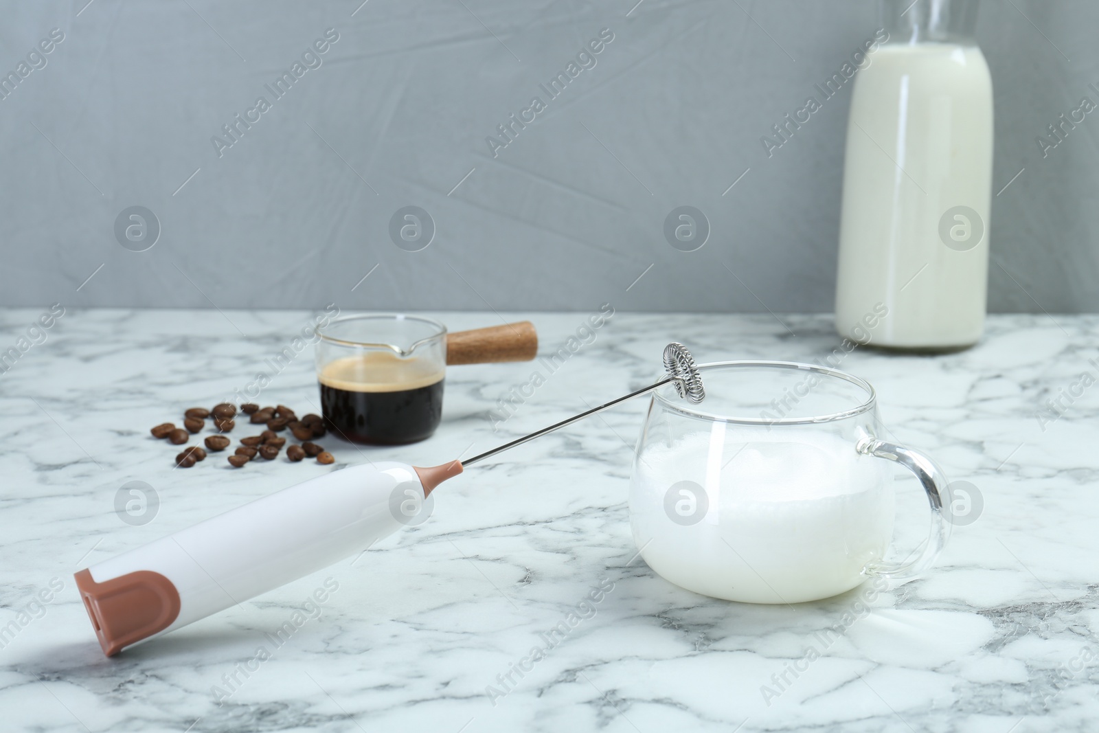 Photo of Mini mixer (milk frother), milk and coffee beans on white marble table