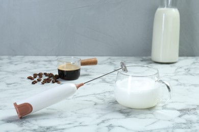 Mini mixer (milk frother), milk and coffee beans on white marble table