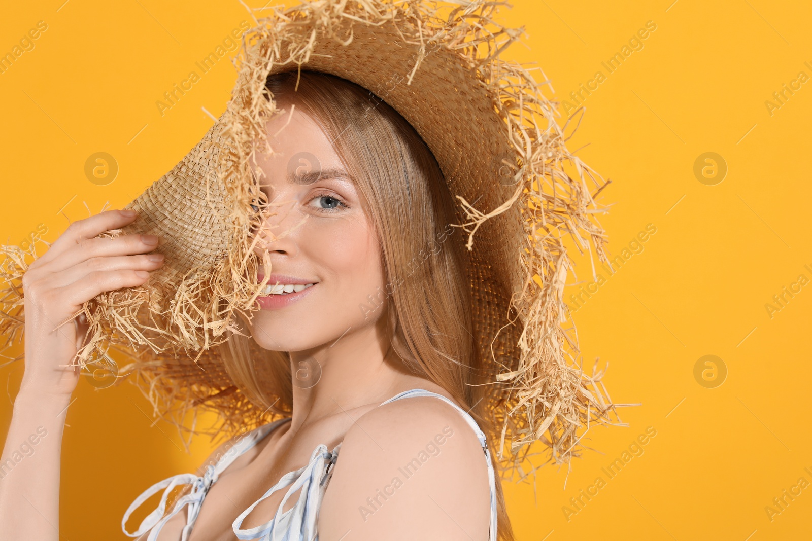 Photo of Beautiful young woman in straw hat on orange background, space for text