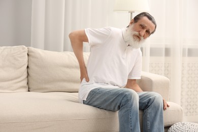 Photo of Senior man suffering from back pain on sofa indoors. Rheumatism symptom