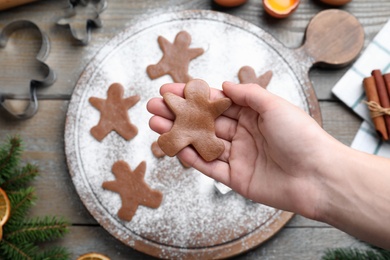 Photo of Making homemade Christmas cookies. Woman holding gingerbread man above wooden table, top view