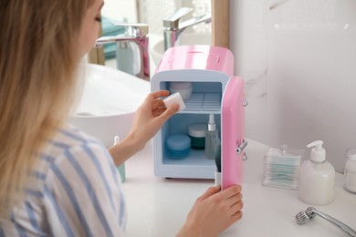 Photo of Woman taking cosmetic product from mini fridge indoors, closeup
