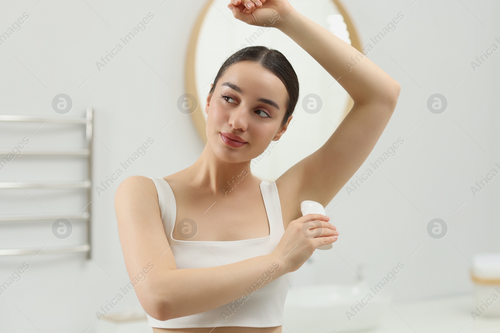 Photo of Beautiful young woman applying deodorant in bathroom