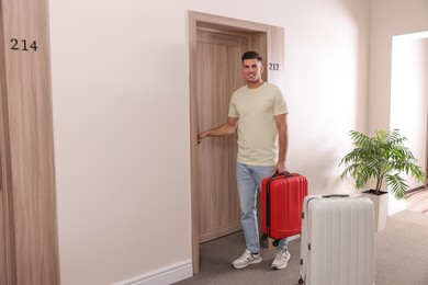 Photo of Happy man with suitcase opening door in hotel