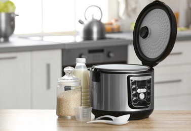 Photo of Modern electric multi cooker, rice and milk on table in kitchen. Space for text