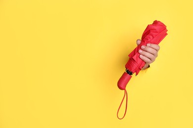 Photo of Woman holding red umbrella through hole in yellow paper, closeup. Space for text