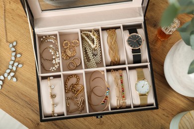 Photo of Elegant jewelry box with beautiful bijouterie and expensive wristwatches near luxury perfume on wooden table, flat lay