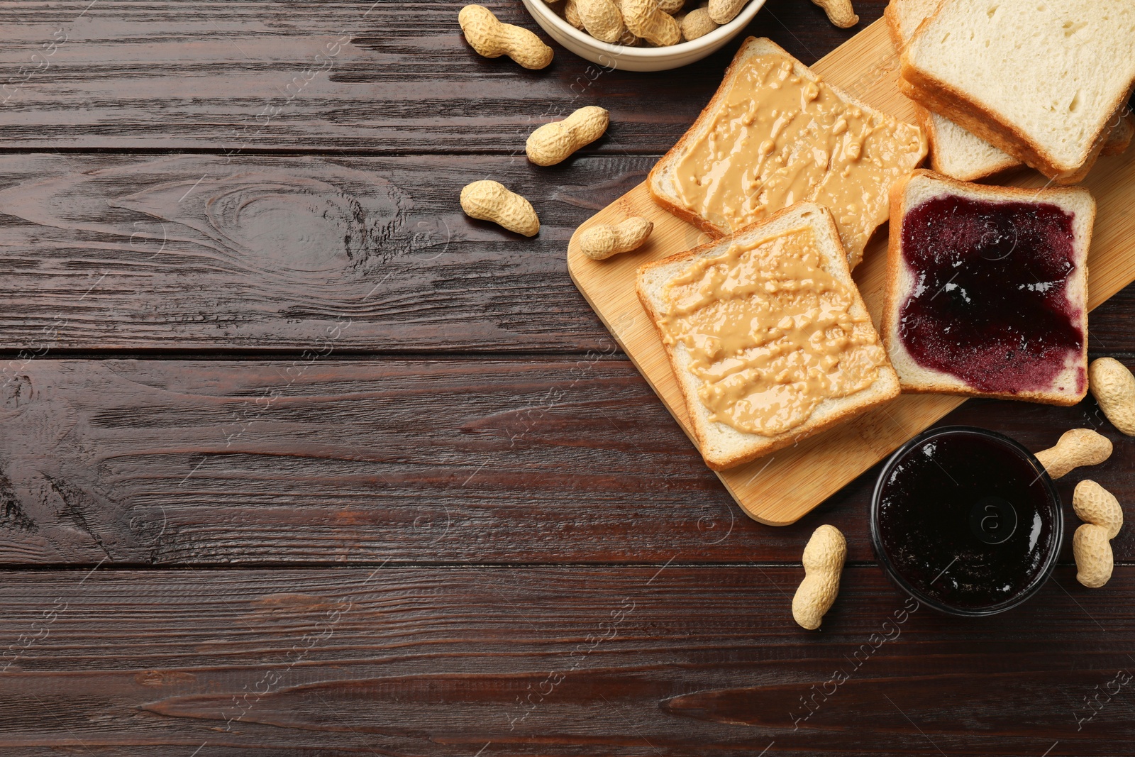 Photo of Delicious toasts with peanut butter, nuts and jam on dark wooden table, flat lay. Space for text