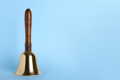 Photo of Golden school bell with wooden handle on light blue background. Space for text