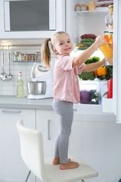 Photo of Cute girl taking bottle with juice out of refrigerator in kitchen