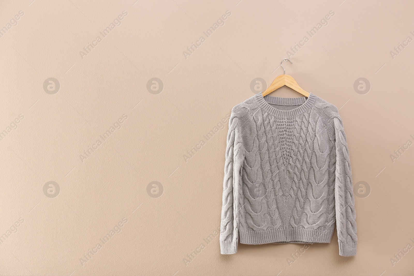 Photo of Hanger with stylish sweater on beige wall. Space for text