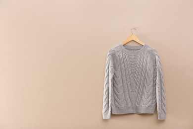 Hanger with stylish sweater on beige wall. Space for text