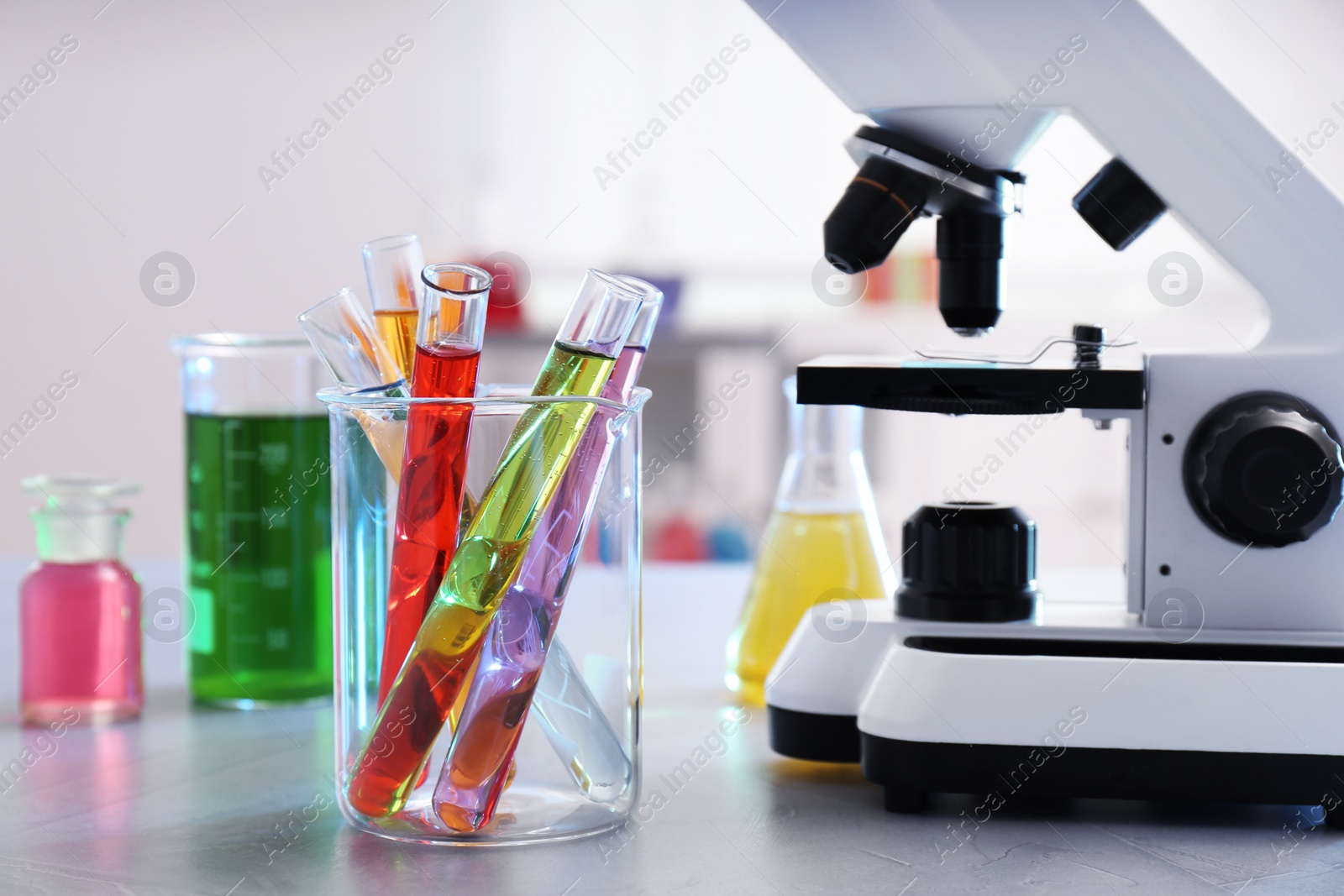 Photo of Beaker with test tubes near microscope on table. Chemistry glassware