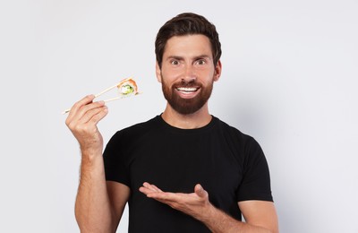 Photo of Happy man holding sushi roll with chopsticks on light grey background