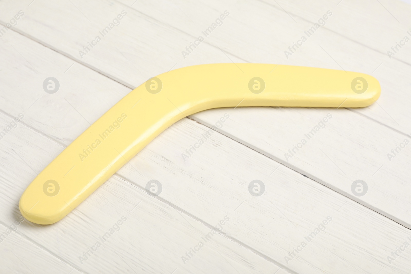 Photo of Yellow boomerang on white wooden background. Outdoors activity