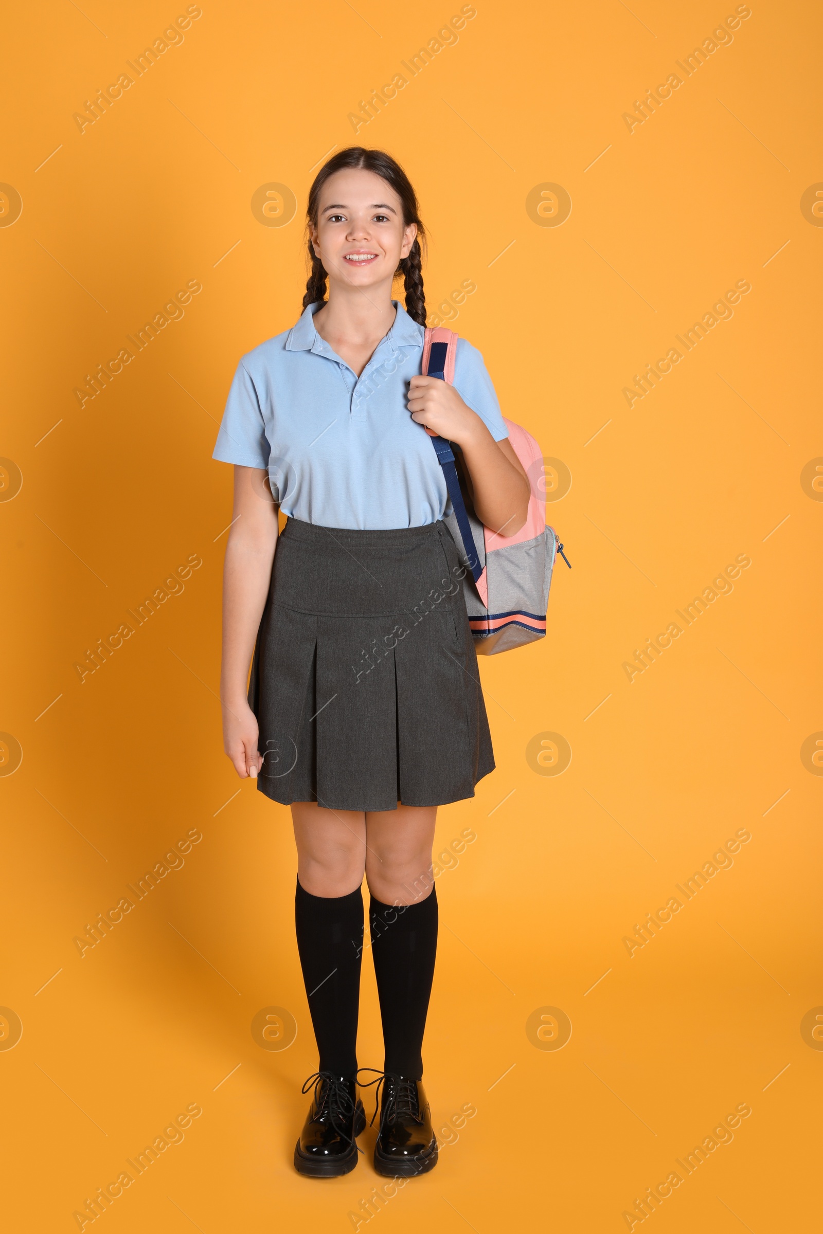 Photo of Teenage girl in school uniform with backpack on orange background