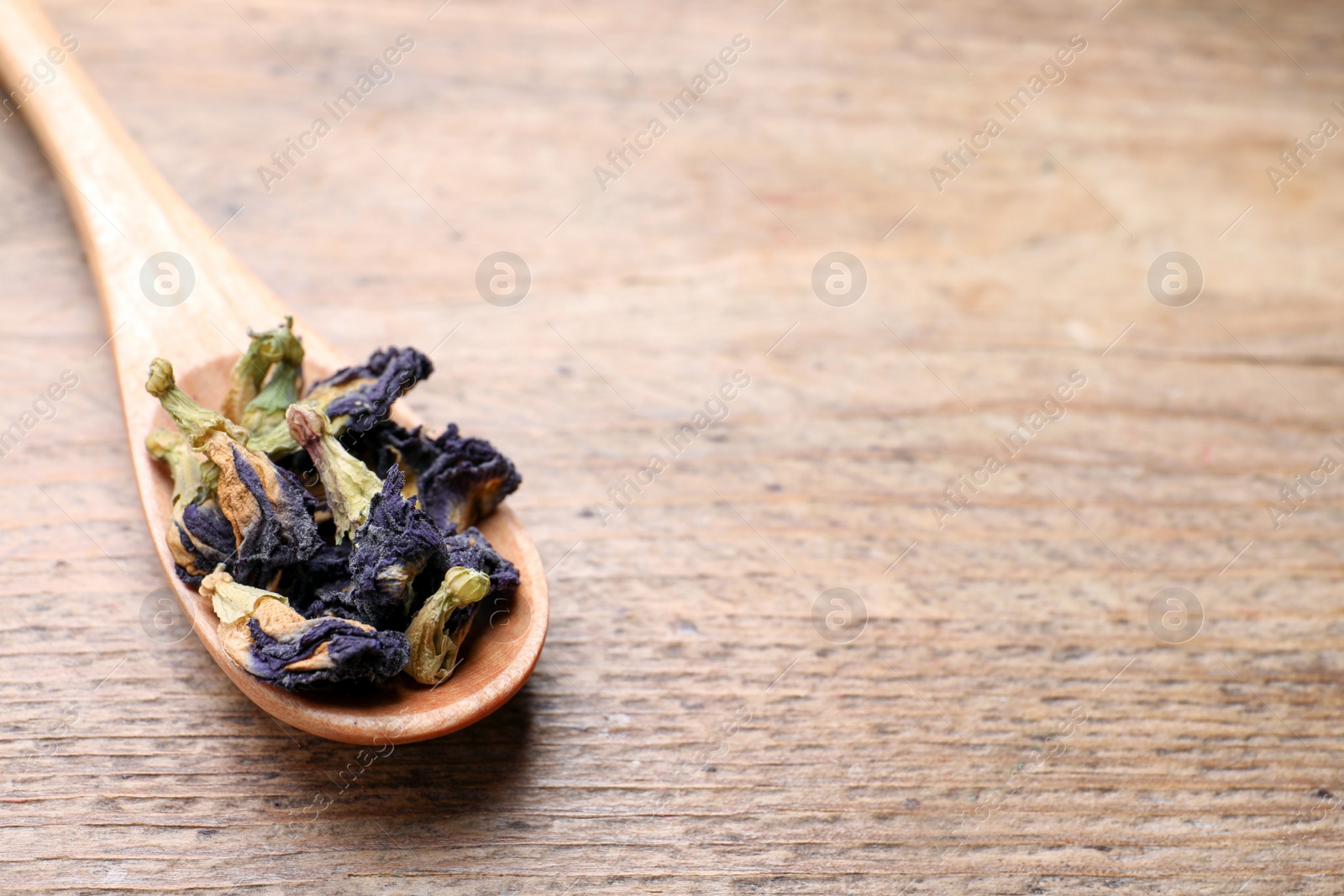 Photo of Spoon with dry organic blue Anchan on wooden table, space for text. Herbal tea