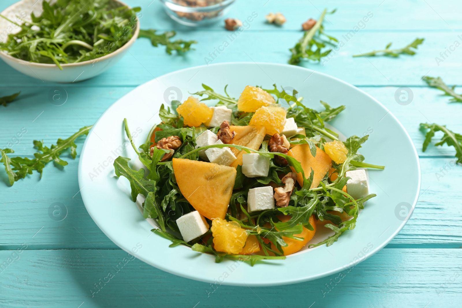 Photo of Delicious persimmon salad with arugula and walnuts on light blue wooden table