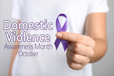 Image of Woman holding purple ribbon on grey background, closeup. Symbol of Domestic Violence Awareness