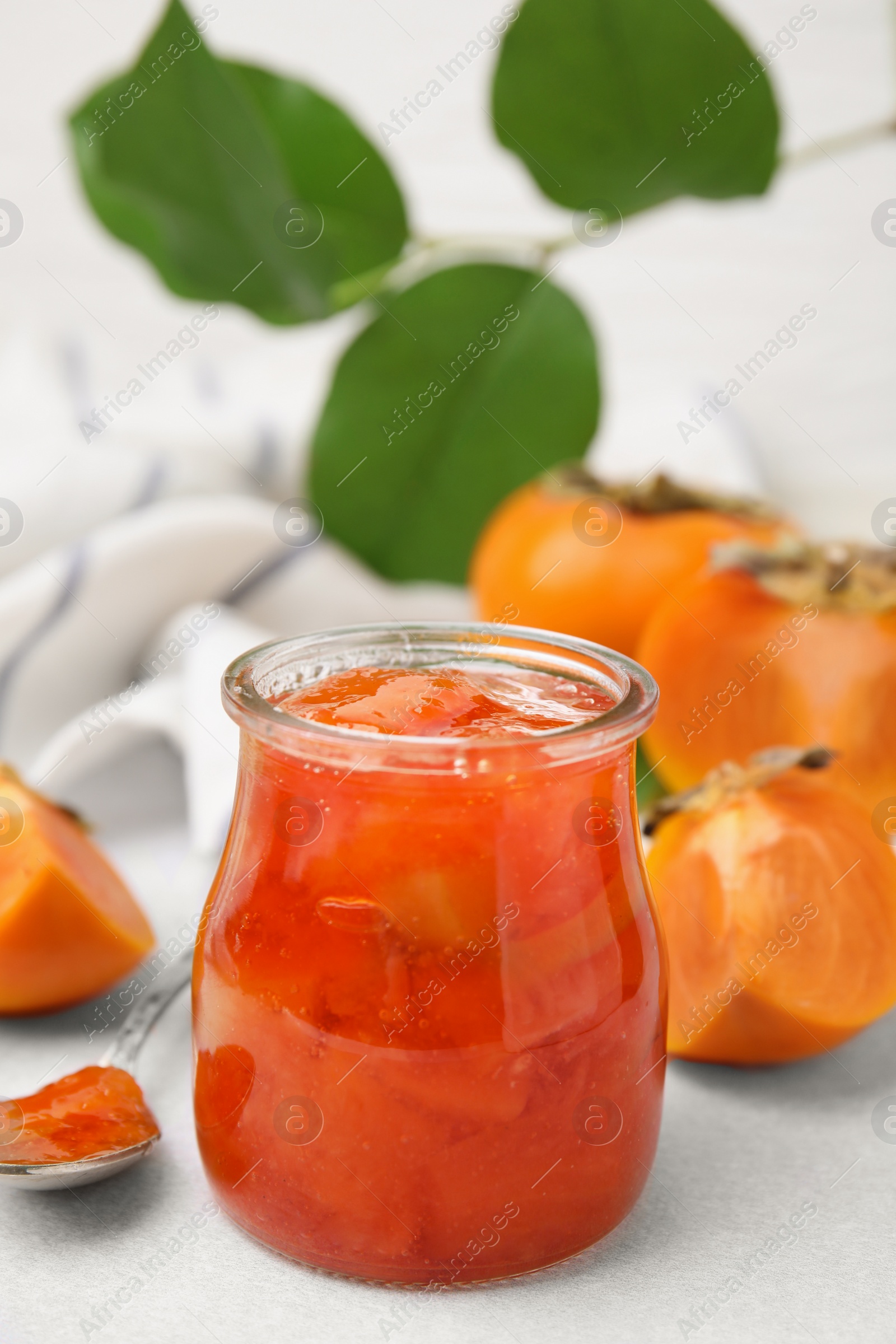 Photo of Jar of tasty persimmon jam and ingredients on white table