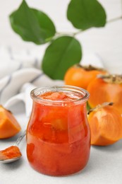 Jar of tasty persimmon jam and ingredients on white table