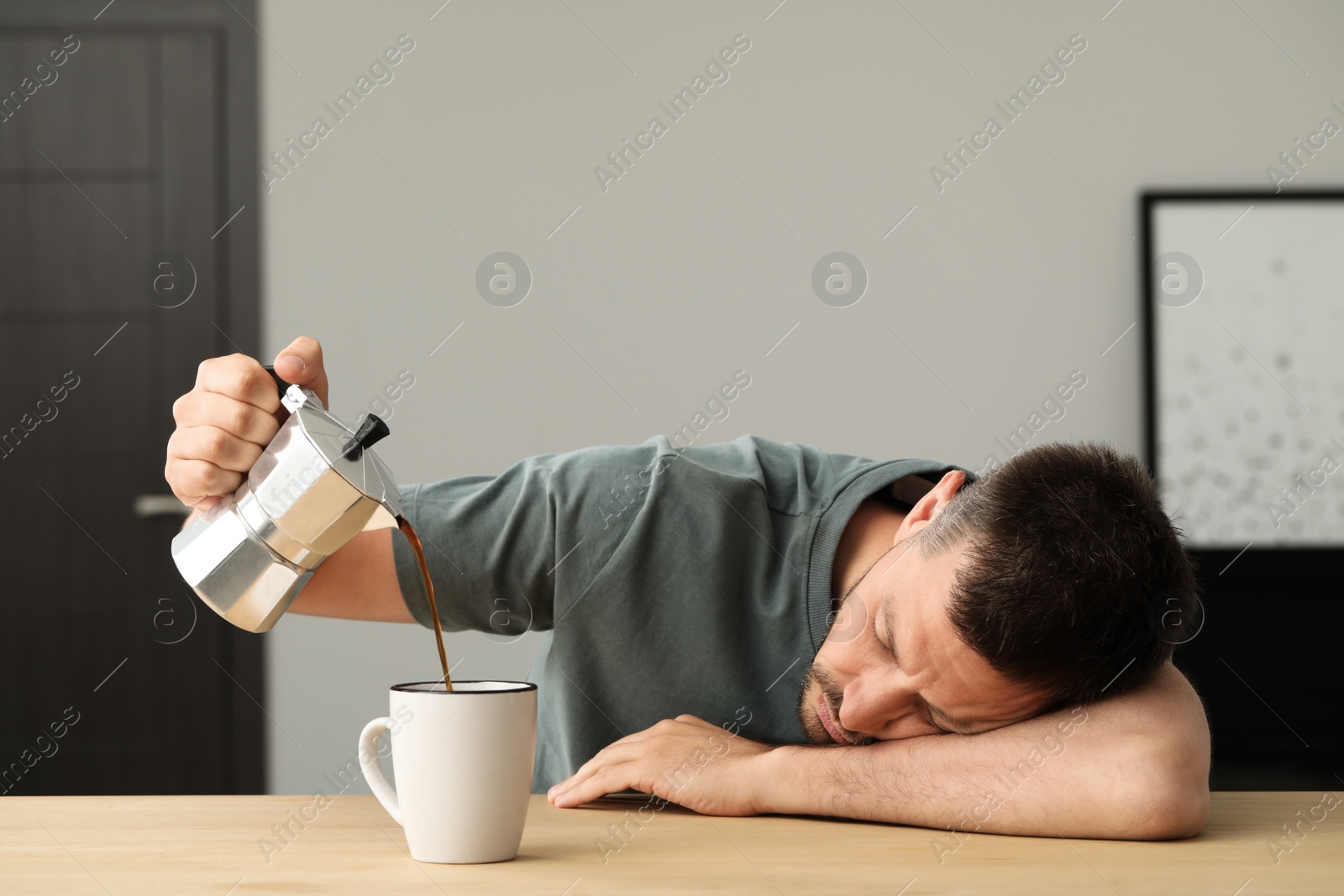 Photo of Sleepy man pouring coffee in cup at wooden table indoors