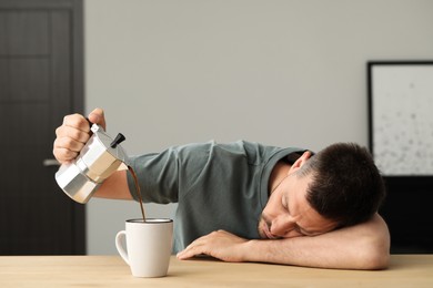 Sleepy man pouring coffee in cup at wooden table indoors