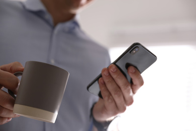 Photo of Man with cup and smartphone against light background, closeup of hands