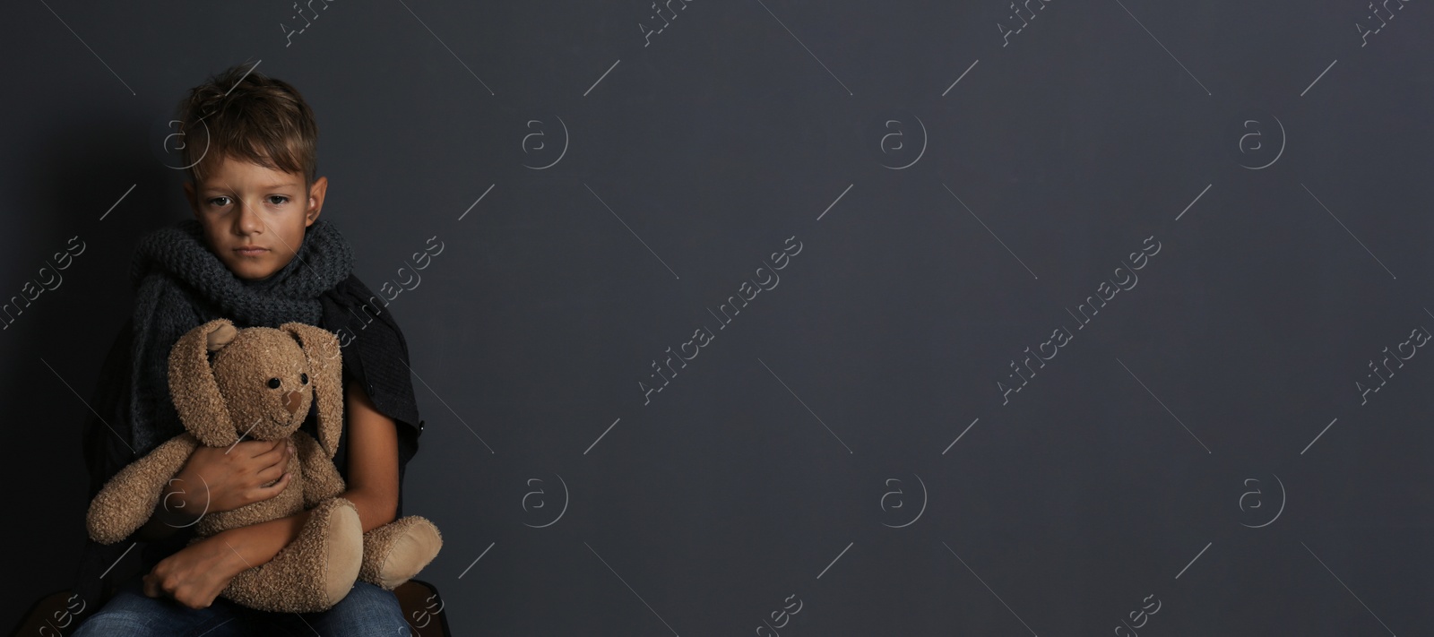 Image of Poor boy sitting with toy rabbit on dark background, space for text. Banner design