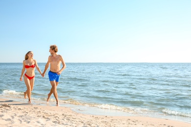 Photo of Happy young couple in beachwear walking together on seashore