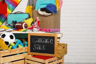 Photo of Sign Garage Sale written on blackboard near many different stuff indoors. Space for text