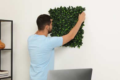 Man installing green artificial plant panel on white wall in room