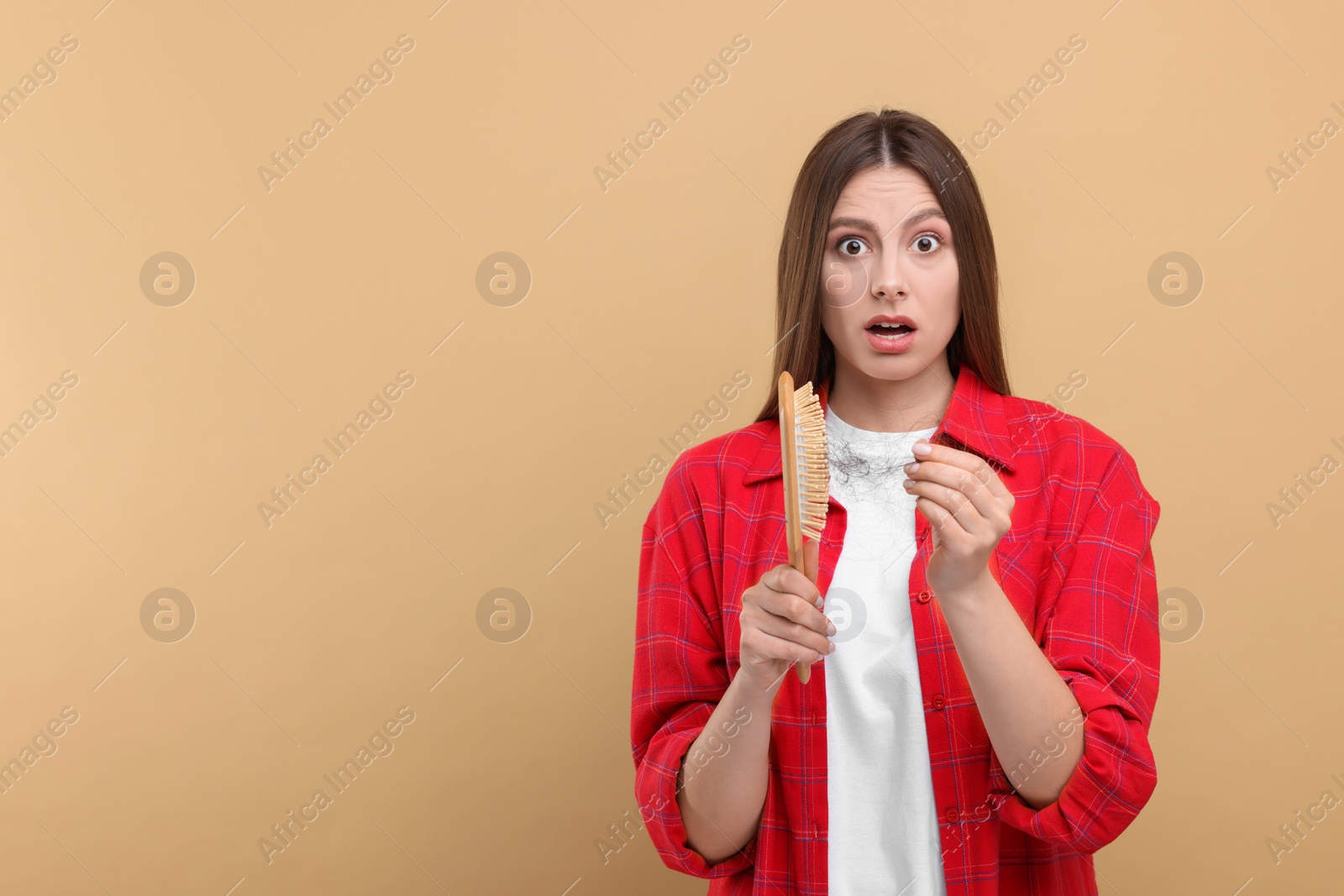 Photo of Emotional woman untangling her lost hair from brush on beige background, space for text. Alopecia problem