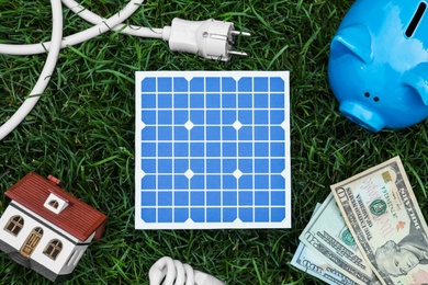 Flat lay composition with solar panel, house model and money on green grass
