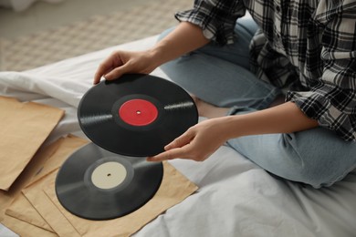 Photo of Young woman choosing vinyl disc to play music with turntable on bed, closeup
