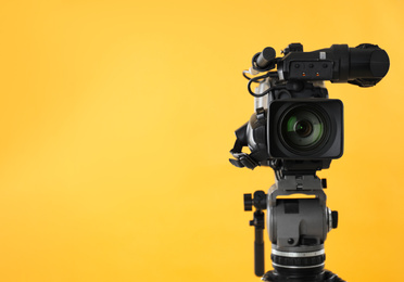 Modern professional video camera on yellow background. Space for text