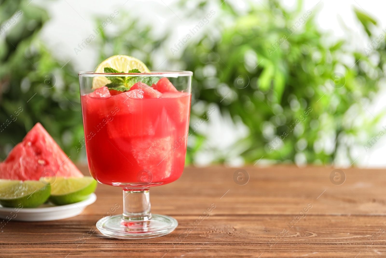 Photo of Tasty summer watermelon drink in glass on table against blurred background. Space for text