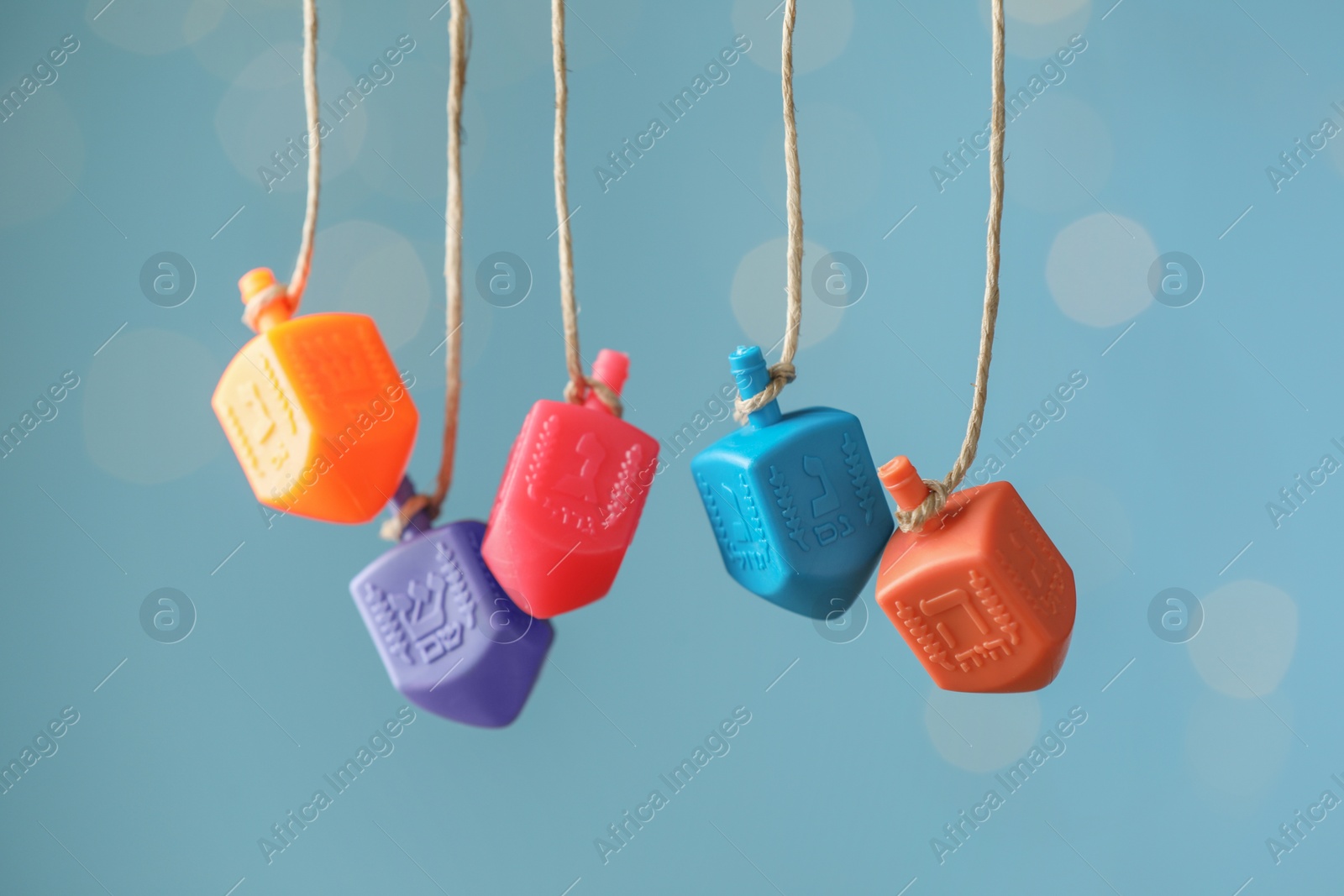 Photo of Hanukkah celebration. Plastic dreidels with jewish letters hanging on twine against light blue background with blurred lights, closeup