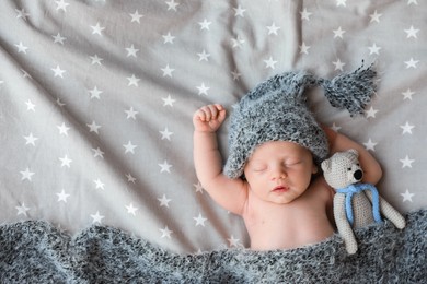 Cute newborn baby in warm hat with toy sleeping on bed, top view. Space for text