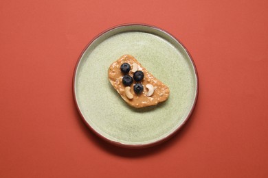 Photo of Toast with tasty nut butter, blueberries and cashews on coral background, top view