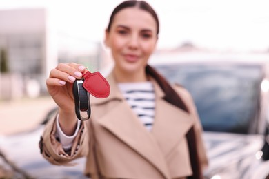 Woman holding car flip key near her vehicle outdoors, selective focus
