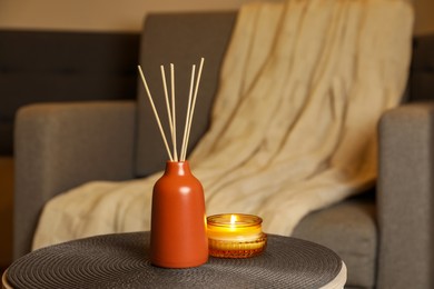 Photo of Aromatic reed air freshener and scented candle on table indoors