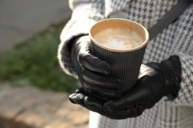 Photo of Woman with coffee in paper cup outdoors, closeup. Space for text