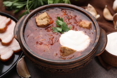 Photo of Tasty borscht with sour cream in bowl served on brown table, closeup