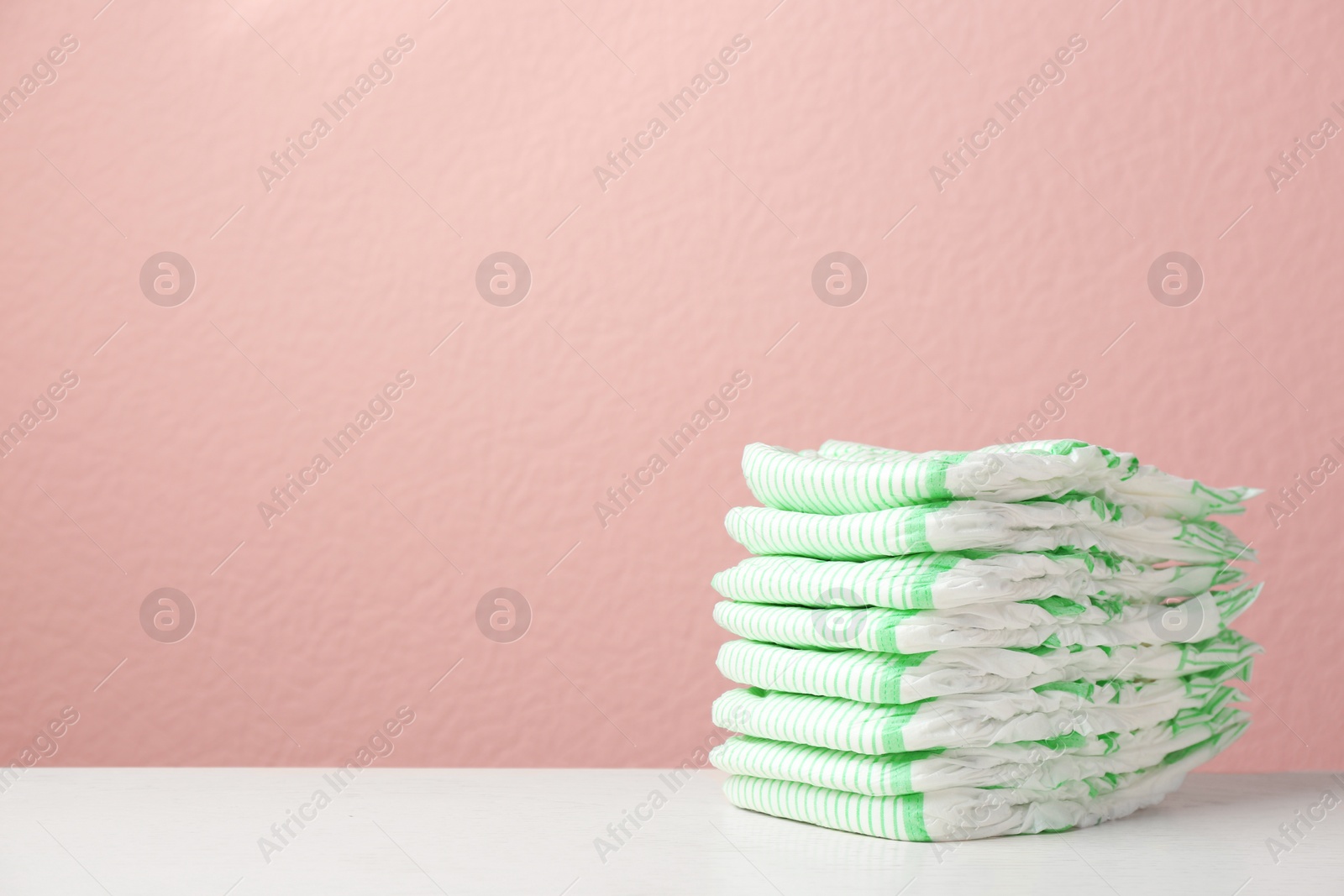 Photo of Stack of diapers on table against color background, space for text. Baby accessories