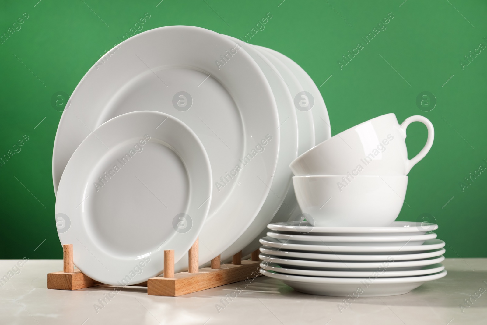 Photo of Set of clean dishware on white table against green background