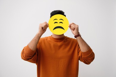 Man hiding behind card with sad face on white background