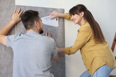 Couple hanging stylish gray wallpaper in room